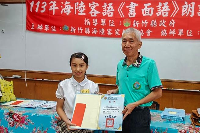 新竹县海陆客家语文协会办理海陆客语《书面语》朗诵比赛，復旦中学附设国中部学生陈姵竹（左）获国高中组第一名，由该协会理事长庄万贵（右）颁发奖金和奖状。（新竹县政府提供／罗浚滨新竹传真）
