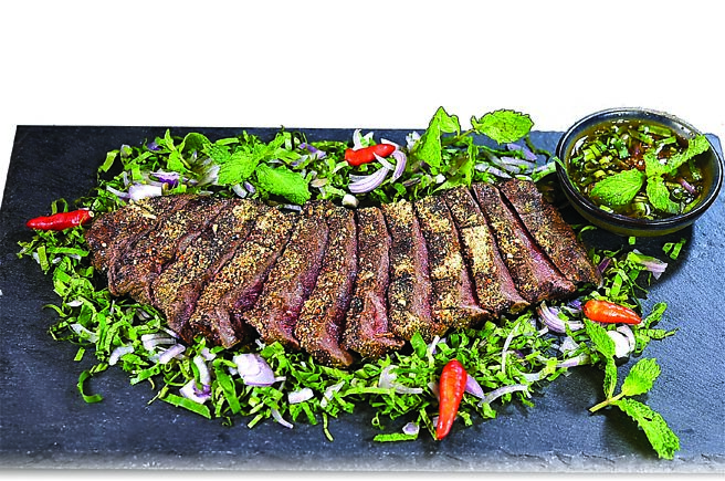 〈碳烤澳洲M9和牛佐泰式香料沙拉〉是以澳洲和牛肋眼腌渍后直火炭烤，撒上与辛香料一起打碎磨成粉的糯米粉，底部衬着凉拌菜。图／姚舜