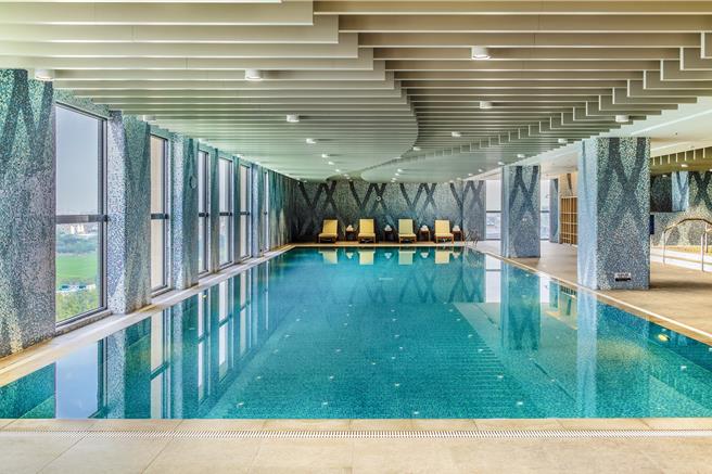 泳池如镜面般的池水映衬着窗外蓝天与平原绿荫，在此游泳就像游进嘉南平原大自然的环抱中。(嘉义福容voco酒店提供)