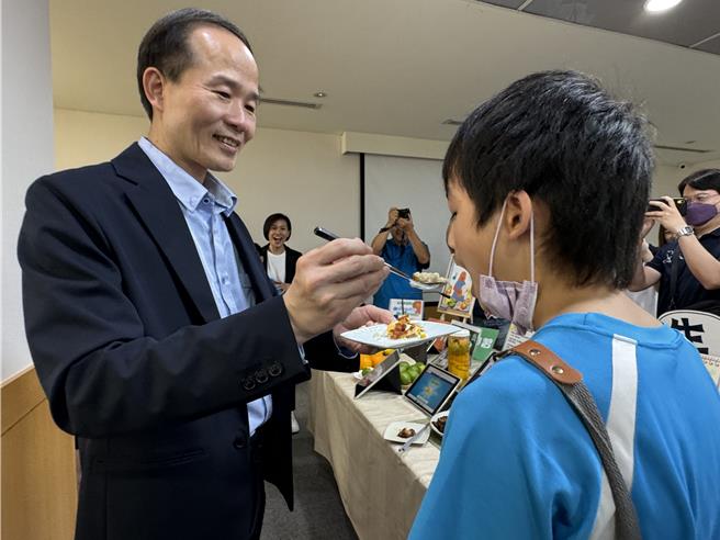 龟山区大坑国小推出家有小厨神，鼓励为亲友下厨，局长刘仲成（左一）见学生做的料理直讚色香味俱全，当场喂食学生。（蔡依珍摄）