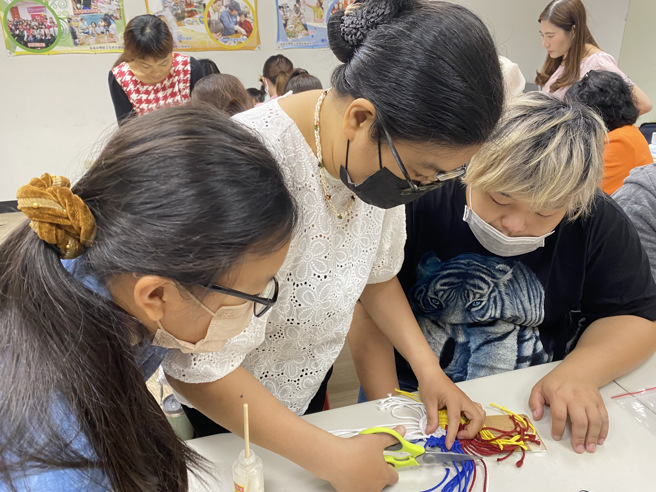 罗戴娜讲师(中)讲解如何制作法式花边杯垫的流苏。(移民署嘉义市服务站提供)