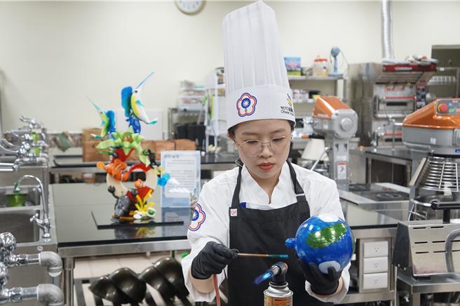 屏科大餐旅系3年级学生陈怡蓁示范吹糖技巧，制作「未来世界」作品组装元素之一的「地球」。（罗琦文摄）