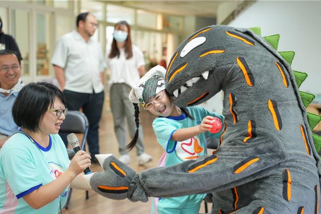 基隆市教育處代理處長楊桂杰26日出席市立安心幼兒園贈書儀式，致贈由市長謝國樑挑選世界知名作家宮西達也創作的兒童繪本。圖為小朋友與「霸王龍」人偶互動。（基隆市教育處提供／徐佑昇基隆傳真）