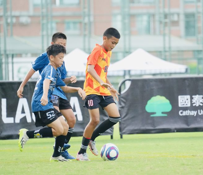 小不老足球俱樂部江孝澤（右）在兩人防守下試圖盤球擺脫。（柏文健康事業提供）