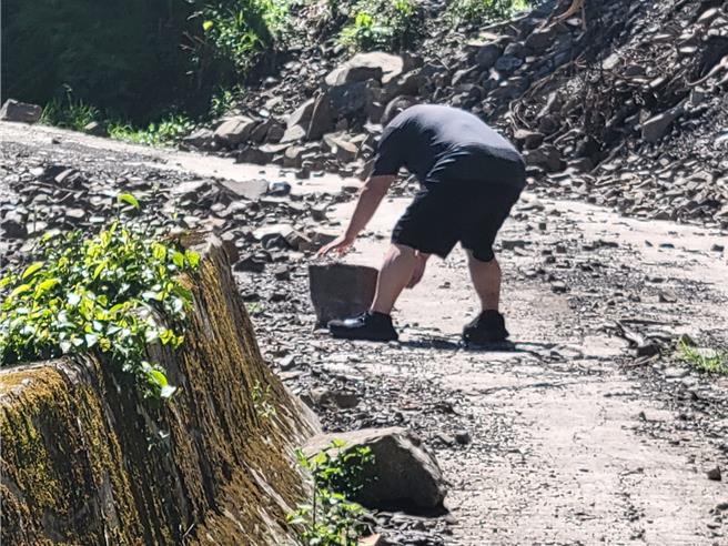 苗栗縣南庄鄉通往鹿湖．鹿山部的301農路受雨勢影響落石坍方不斷，南庄鄉代表風志雄下車搬移落石。（苗栗縣議員楊文昌提供／謝明俊栗傳真）