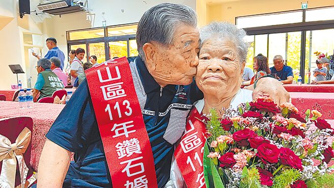 台南市東山區東山里的蘇西華（左）、蘇張檖月（右）夫妻14日在東山國小文教活動中心獲表揚為鑽石夫妻，蘇西華在鏡頭前放閃，親吻太太臉頰。（張毓翎攝）