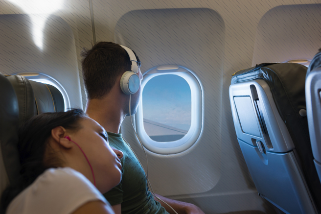 手機、平板電腦普及，常可見到戴著耳機的旅客在飛機上使用行動裝置聽音樂、看影片。（示意圖：shutterstock／達志）
