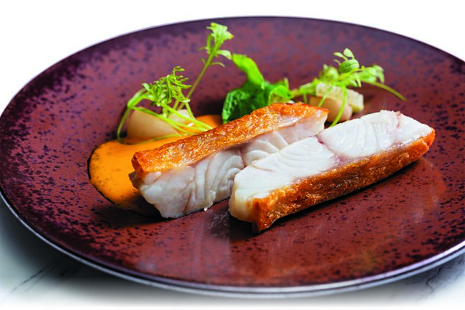 A CUT牛排館本季「季節鮮魚」，是以經過鹽浴法處理的石斑魚香煎後，搭配馬賽魚醬汁，飄著濃郁熟成番茄與海鮮香氣，微辣的刺蔥與蔬菜甜口的尾韻相得益彰。圖／A CUT  STEAKHOUSE