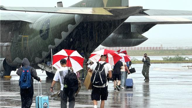 今日金門機場天雨不斷，歸心似箭的滯留旅客拿著金防部官兵提供的傘具，快速登機。(于家麒攝)