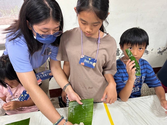 圣约翰王亭雅同学（左一）向小朋友示范怎么包香蕉粽。(照片/圣约翰科大提供)