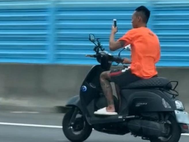 民眾拍下1名橘衣男骑机车上国道，未戴安全帽，且边骑车边玩手机。（民眾提供／孙英哲彰化传真）