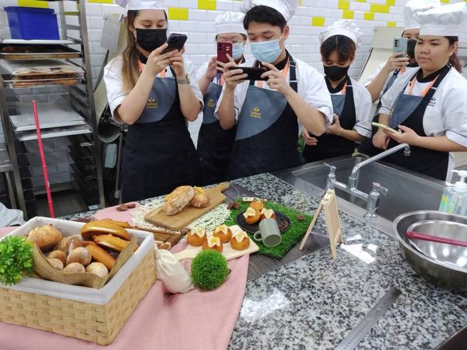 康豐柚師傅示範製作傳統法國麵包、辣椒卡門貝爾、德式扭結麵包與雙乳酪鹼水包，色香味俱全令人垂涎三尺，馬來西亞學員仔細拍照研究製作竅門。(照片/醒吾科大提供)