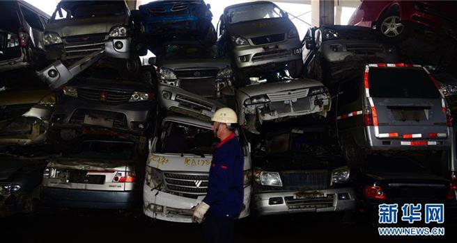 工人从广州市金属回收有限公司购销部堆放的报废汽车前走过。（图／新华社资料照）
