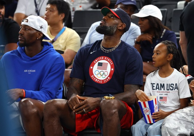 詹姆斯(中)膝蓋放著男籃金牌觀看女籃金牌戰。(路透)