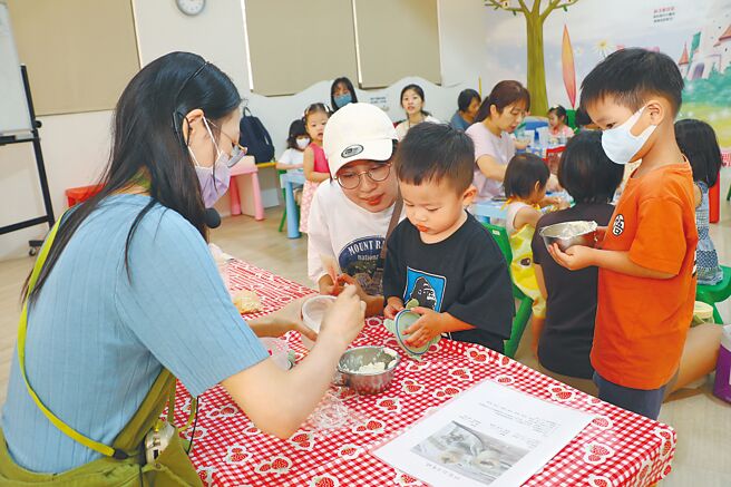新北市三重重新公托親子館親子廚房的小鹿老師（左）指導參加課程的家長與小朋友製作杯子蛋糕。（呂健豪攝）