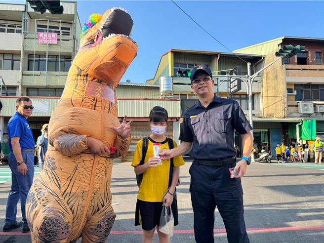 埔心國小教職人員特意扮演恐龍，在校門口迎接活潑可愛的小朋友，員警執行「護童專案勤務」，並發送文具宣導品，拿到的學生露出笑顏，開心上學。（民眾提供／葉靜美彰化傳真）
