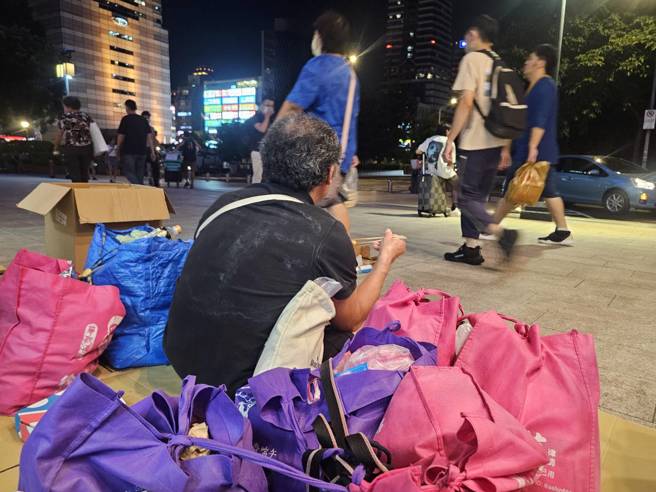 赖先生身边不少家当，与繁华街道形成强烈对比。（记者游定刚拍摄）