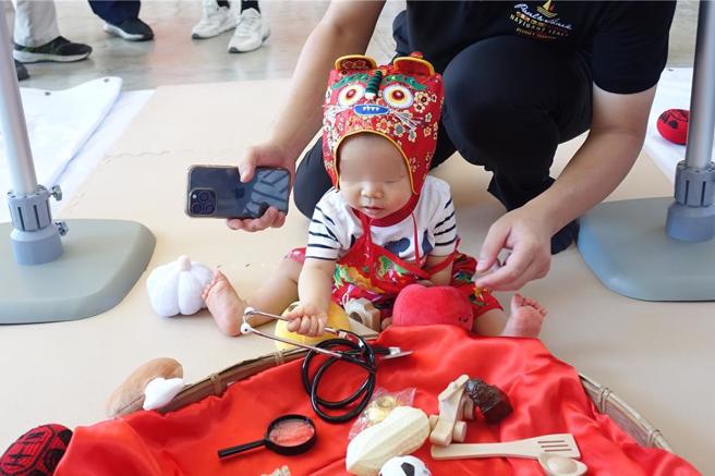万峦抓周迎新丁新枝，小宝宝穿着虎衣虎帽，抓起听诊器。（罗琦文摄）