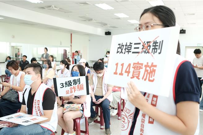 大新竹高中就學權益自救會9日在竹北市中興里集會所開會，自救會成員和家長持「改掉三級分制，114實施」等手舉牌。（羅浚濱攝）