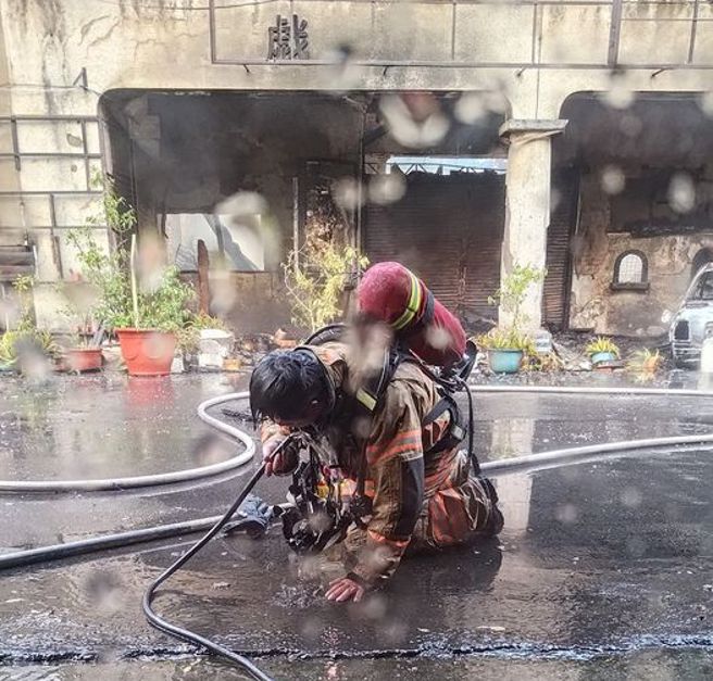 有网友拍下一名消防人员跪在地上，并用水管浇灌身体试图降温，画面经网路曝光后掀起热议。（图 / 翻摄自脸书社团「路上观察学院」）