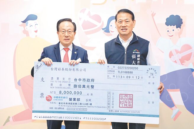台灣彩券公司董事長黃志宜（左）代表大樂透頭獎中獎人，將象徵800萬元的大型支票捐贈給台中市政府，由市府副祕書長張大春（右）代表受贈。（林欣儀攝）