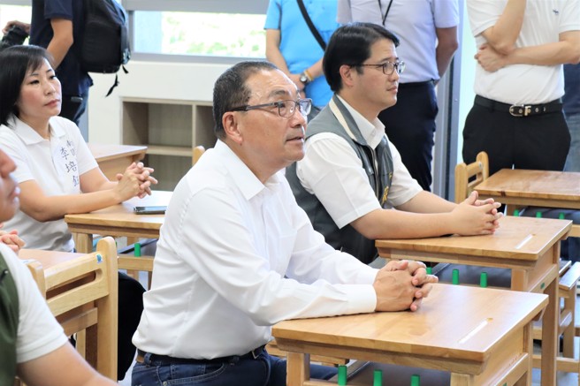 市長侯友宜至北大特區桃子腳國中小視察校舍完工，與多位民代一起坐在新教室中模仿學生上課般，聽取校長簡報。圖/新北市政府提供