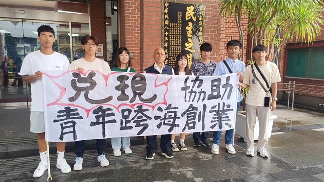 金门县议会第8届第8次临时会今日进行金酒厦门公司大陆总经销规划案专案报告；开议前，议员李养生( 左四 )与7名青年却在议会大门口拉起白布条高喊「要工作」、「要创业」，意外成为场外焦点。（图／民眾提供）