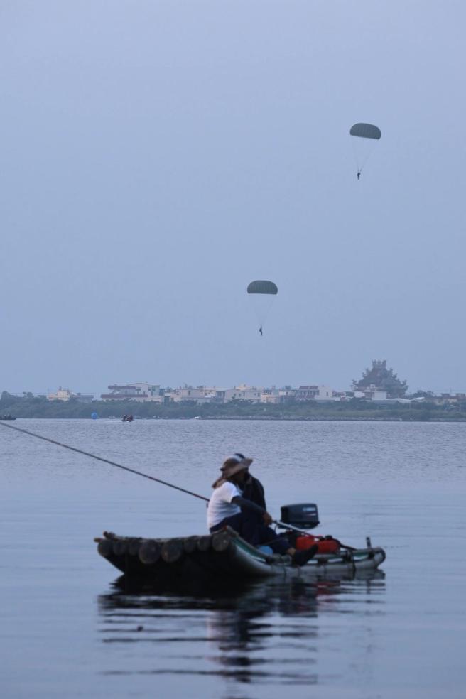 訓員水域跳傘訓練與大鵬灣內晨起釣魚民眾畫面，相映成趣。（記者孫建屏攝）
