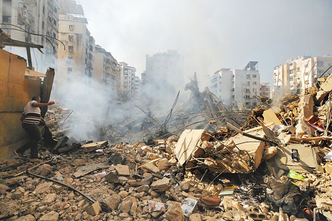 以色列空袭黎巴嫩贝鲁特南部郊区后，28日一名男子走在受损建筑物的废墟上。（路透）