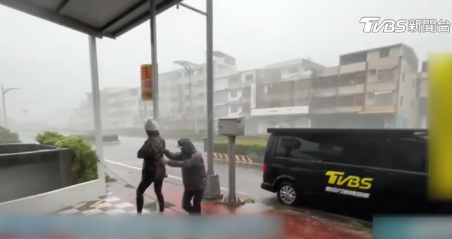 TVBS记者宋佩文和SNG团队前往高雄鼓山採访，但山陀儿风雨强劲，记者只能躲到骑楼下，并抓住支柱才能稳住身体。 （图／摄自YT@TVBS NEWS）