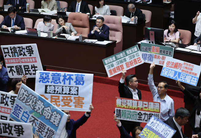 針對中央政府總預算案，立法院4日院會表決，藍白以人數優勢在表決中通過民眾黨團提案，總預算再度遭到退回程委會，民進黨與國民黨立委各舉標語表達立場（姚志平攝）