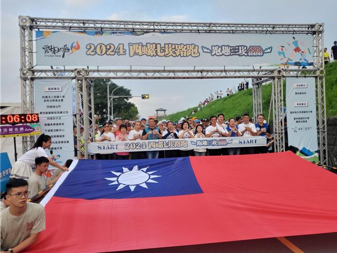 西螺七崁路跑6日登场，为庆祝国庆出发前抬出巨幅国旗合影纪念。（周丽兰摄）