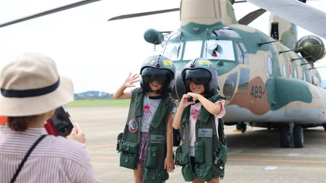 自衛隊在CH-47J運輸直升機機首貼上擬人的雙眼，讓嚴肅的軍事風格裝備，轉眼成為平易近人的軍機，讓孩童爭相戴上飛行頭盔與之合影。（記者謝宗憲攝）