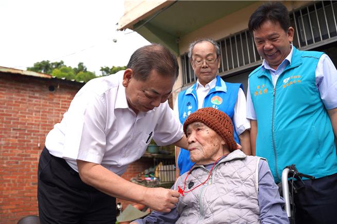 新竹縣副縣長陳見賢（左）替住在關西鎮101歲的余梅見戴上金鎖片。（新竹縣府提供／邱立雅竹縣傳真）