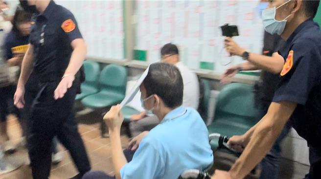 台中市前刑警大队长林明佐遭检方以涉嫌泄漏侦查秘密、收贿及财产来源不明等罪嫌提起公诉，台中地院9日开程序准备庭审理，林明佐坐轮椅、拿文件资料挡住脸进入法庭。（冯惠宜摄）