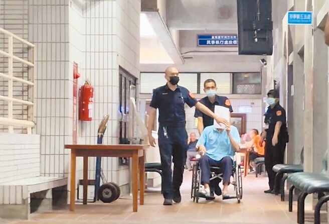 前刑事局高官林明佐涉嫌貪汙洩密案，林明佐（前右）坐輪椅、拿文件資料擋住臉進入法庭。（馮惠宜攝）