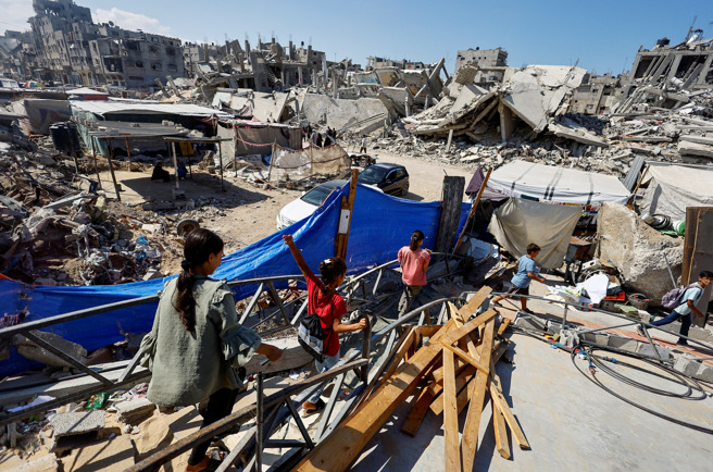 2024年10月，在加萨部汗尤尼斯，以色列与哈玛斯衝突期间，巴勒斯坦学生在穆斯塔法(Israa Abu Mustafa) 的废墟上搭起的帐篷里走路去上课。（路透社）