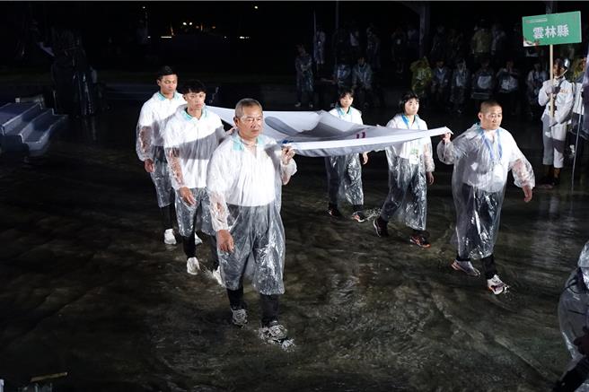 全民運動會昨晚在雨中開幕，大會旗踩水進場。（羅琦文攝）