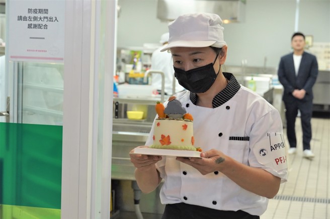 第6屆APPGU寵物烘焙師職業技能大賽初級組第一名的楊玉鈴，以嚴謹的態度，將用時三小時的作品，小心翼翼送至展示區等待評審點評。(照片/吾限熊報社鄭伃媗攝)