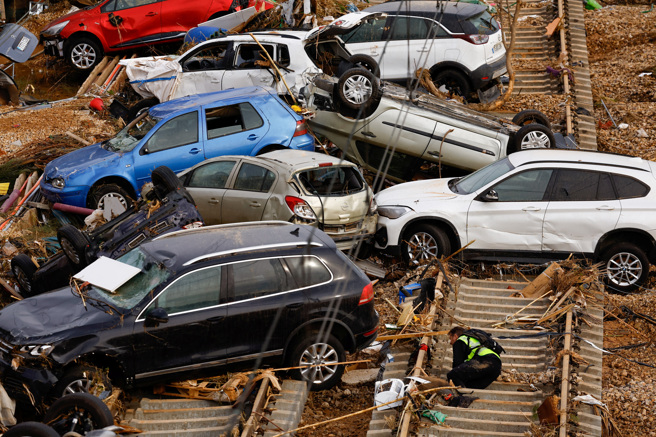 一名消防队员1日在瓦伦西亚省城镇阿尔法法尔（Alfafar）堆积如山的毁损汽车周围搜寻罹难者。（路透）
