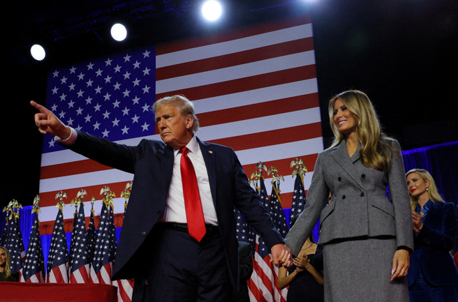 2024年 11月6日，美国佛罗里达州棕榈滩郡会议中心，川普在集会上与妻子梅兰妮亚握手时做出手势。（路透社）