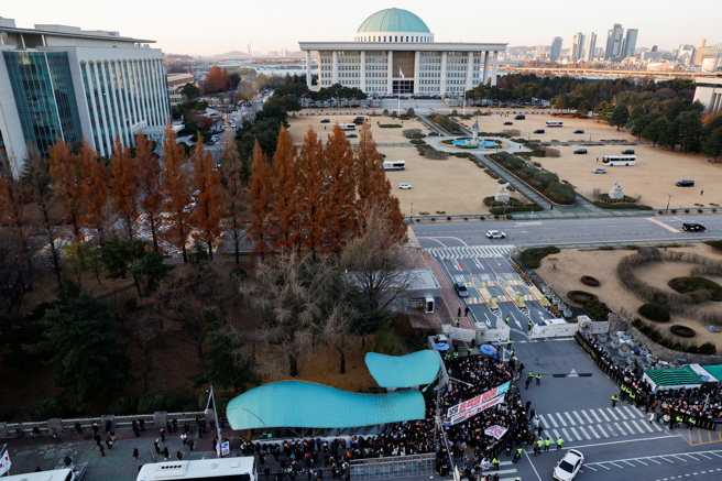 南韓國會主廈草坪、廣場6日停放巴士車輛，以防3日深夜戒嚴部隊搭乘直升機空降國會的場面重演。正門口聚集大批要求總統尹錫悅下台的抗議群眾。（路透）