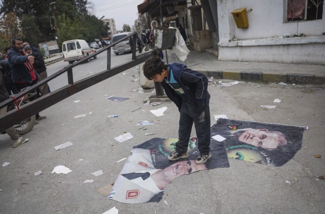 一名叙利亚男孩踏过统治该国50年的两位总统：已故的哈菲兹阿萨德；以及其子巴沙德阿萨德。(图/美联社)