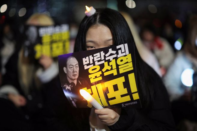 一名抗议者举着写有「逮捕叛乱领导人尹锡烈」的牌子，同时参加在国民议会前举行的集会，呼吁弹劾韩国总统尹锡烈。（图／路透）