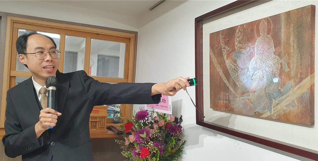 華梵大學佛藝系主任陳俊吉用手電筒導覽作品〈菩提現光明雲〉。（華梵大學提供）