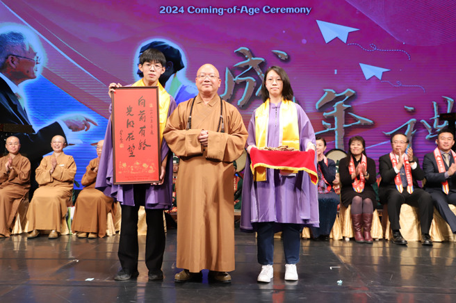 南华大学于佛光山佛陀纪馆举办成年礼，佛光山宗长心保大和尚(中)致赠星云大师2025年墨宝春联「向前有路，光明在望」及佛珠予受礼者。(照片/南华大学提供)