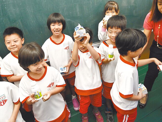 台北市5日率先宣布下學期續辦，不過，晚間卻發新聞稿強調須待中央經費補助到位，最快4月上路。圖為文山區永建國小學生們開心拿著剛領到的乳品。（本報資料照片）