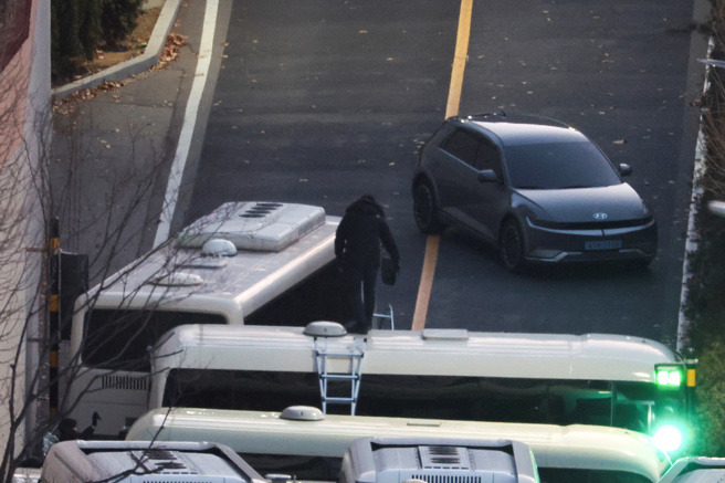 图为设置在尹锡悦官邸大门的大巴车墙，有人爬梯越过车墙，进入官邸园区。（路透社）