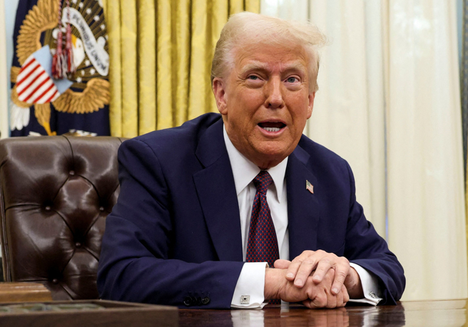 美国总统川普23日在白宫椭圆形办公室签署行政命令的神情。（路透）