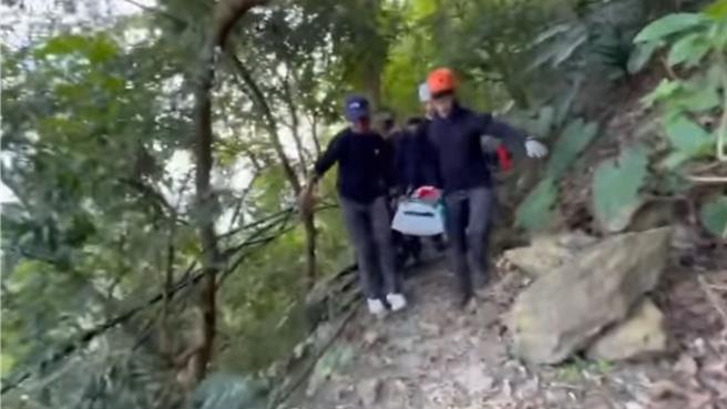 76岁许姓男子登棚集山，不慎滑落10公尺边坡，左肩骨折无法行走，搜救人员以担架将许翁抬下山，登山步道崎岖狭窄，搜救人员抬着担架行走困难。（屏东县消防局提供／罗琦文屏东传真）